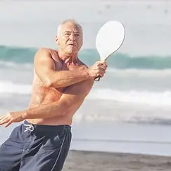 Older Shirtless man playing paddleball on beach