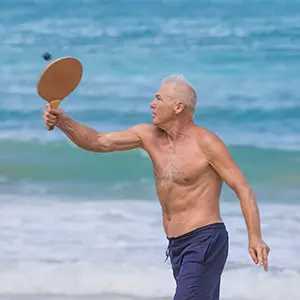 Older Shirtless man playing paddleball on beach